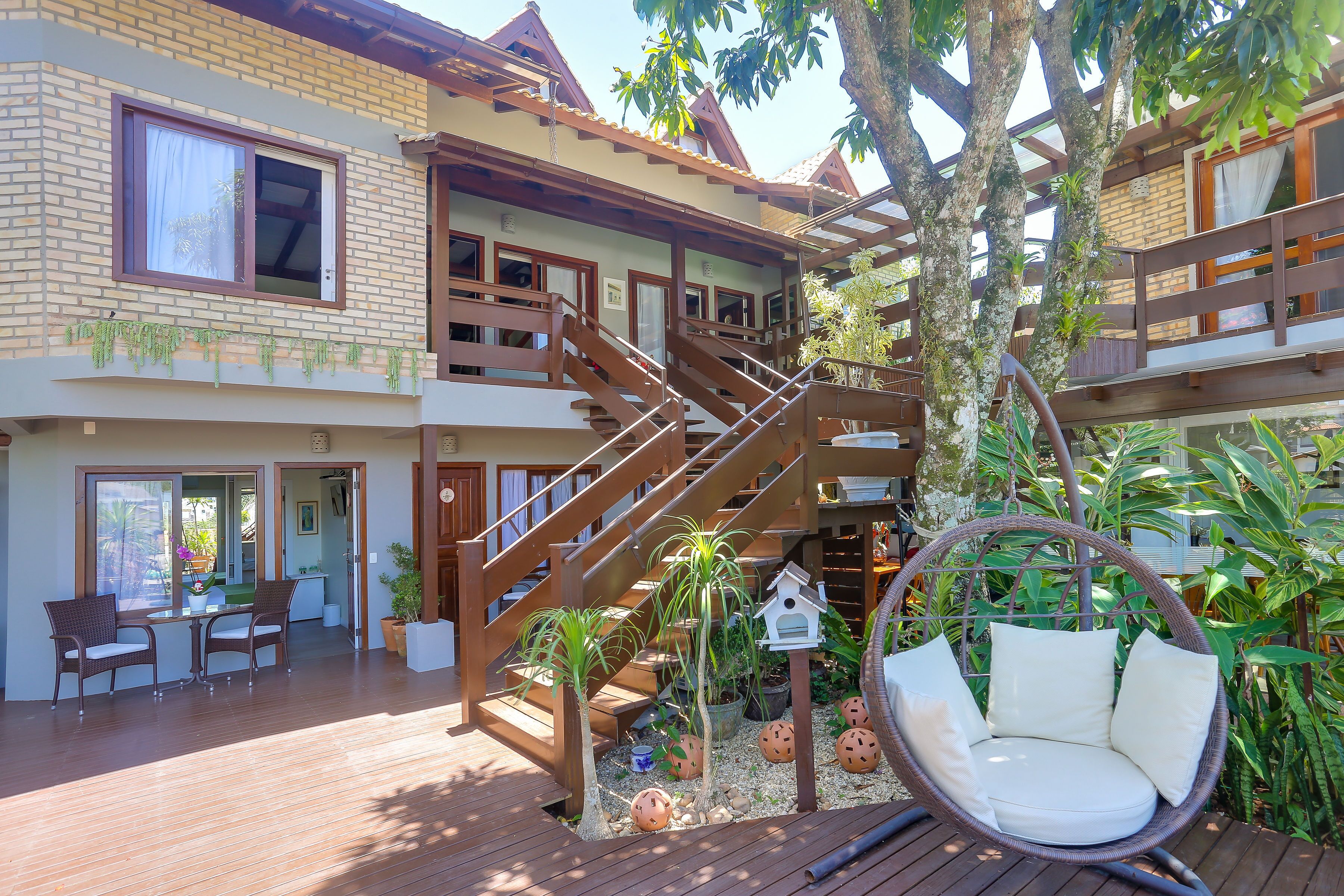 A multi-story house with a wooden deck, outdoor seating, and a hanging chair.