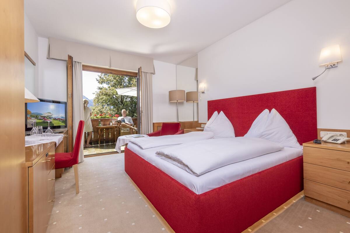 Ein Hotelzimmer mit einem großen Bett, einem Schreibtisch mit Stuhl, einem Fernseher und Blick ins Freie.