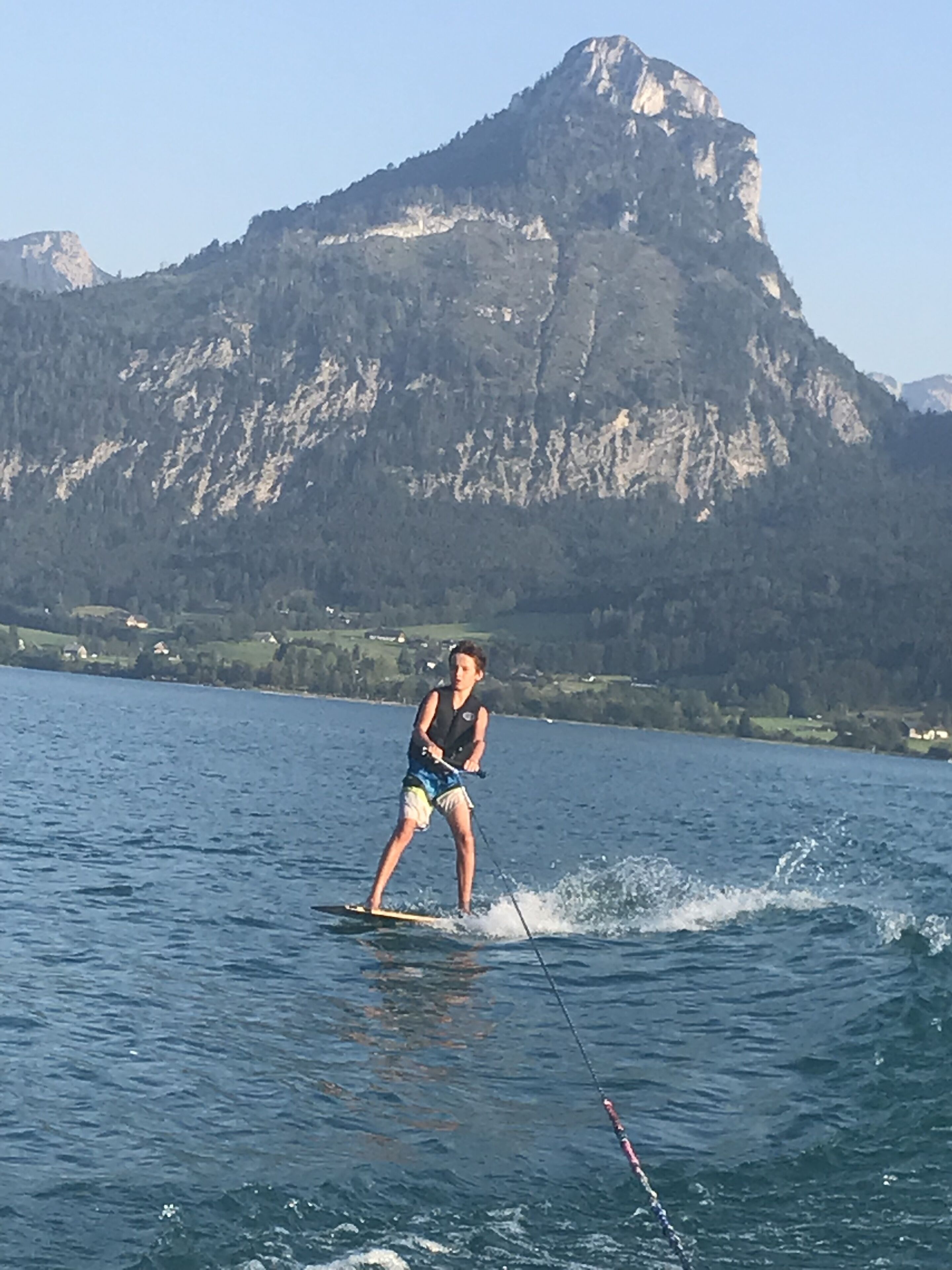Una persona practicando wakeboard en un lago con montañas al fondo.