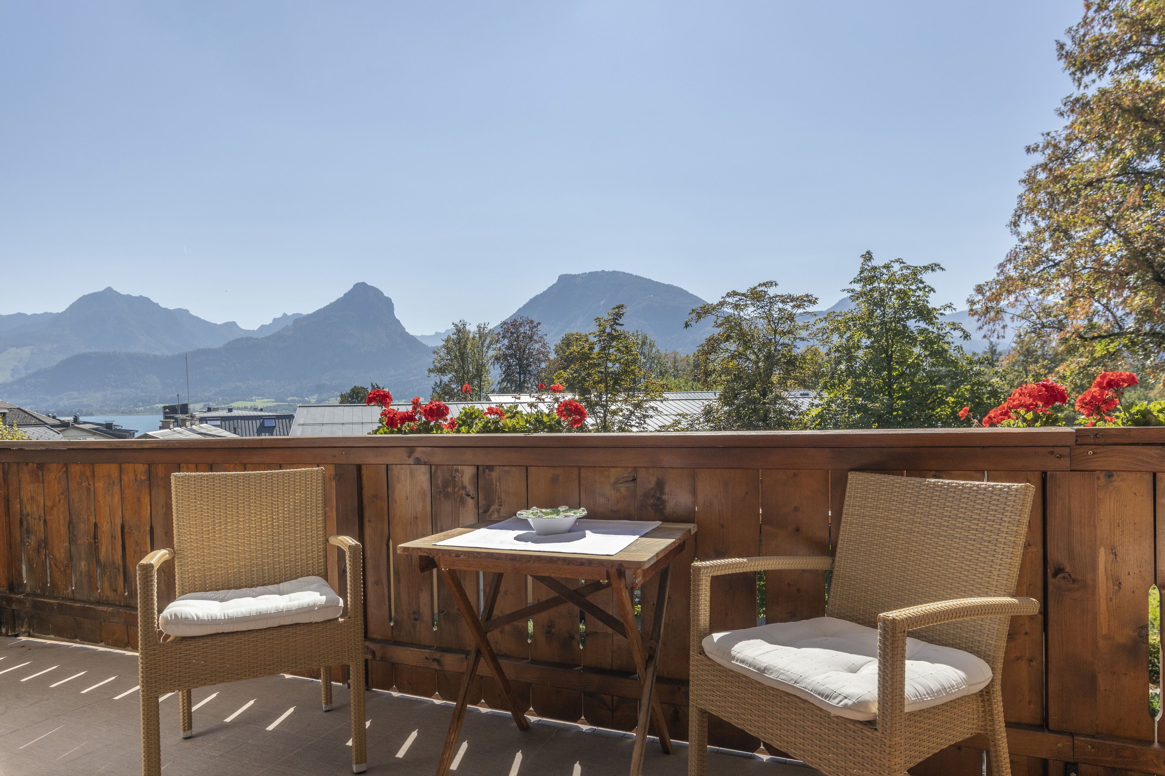 Une terrasse en bois, agrémentée de chaises et d’une table en osier, qui offre une vue sur un paysage montagneux.