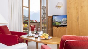 A hotel room with a wooden dining table, red chairs, a television, and a view of mountains through a large window. - Hotel Furian (Sankt Wolfgang im Salzkammergut)