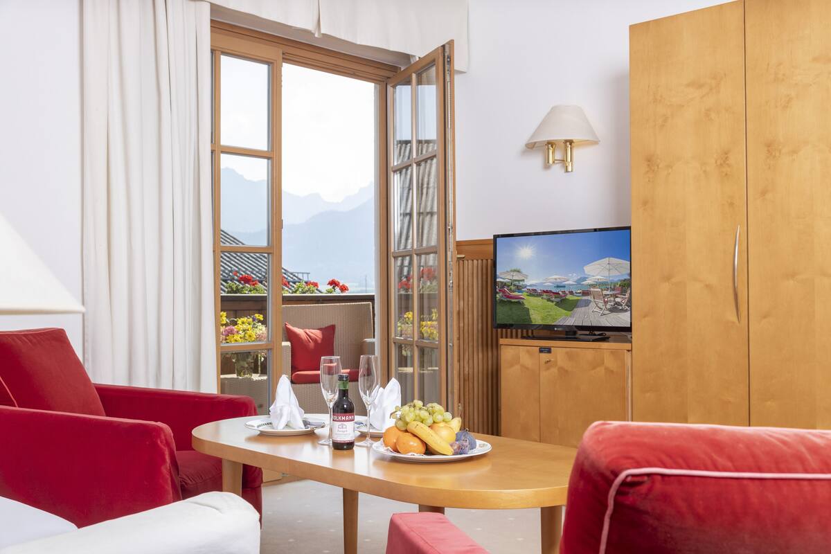Ein Hotelzimmer mit einem Holztisch, roten Stühlen, einem Fernseher und Bergblick durch ein großes Fenster.