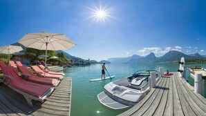 A wooden pier with lounge chairs and umbrellas, a paddleboarder, and boats docked. - Hotel Furian (Sankt Wolfgang im Salzkammergut)
