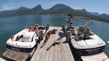 A wooden dock with two boats, one with skis and another with a canopy, docked at a lake with mountains in the background.
