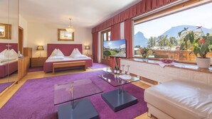 A modern hotel room with a bed, a sofa, a glass coffee table, and a large window with a mountain view. - Hotel Furian (Sankt Wolfgang im Salzkammergut)