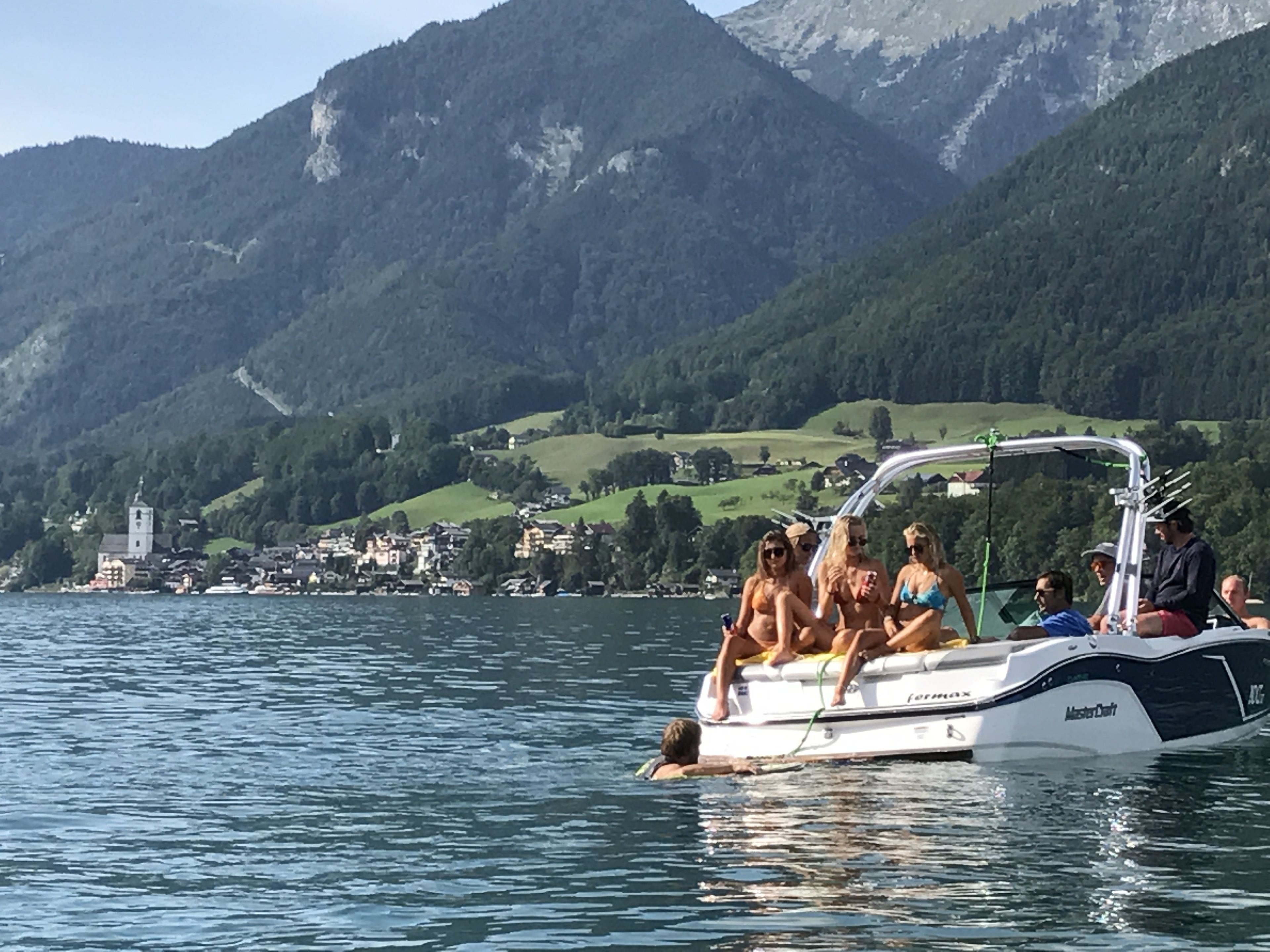 Een boot met passagiers op een meer, omringd door bergen en een klein stadje.