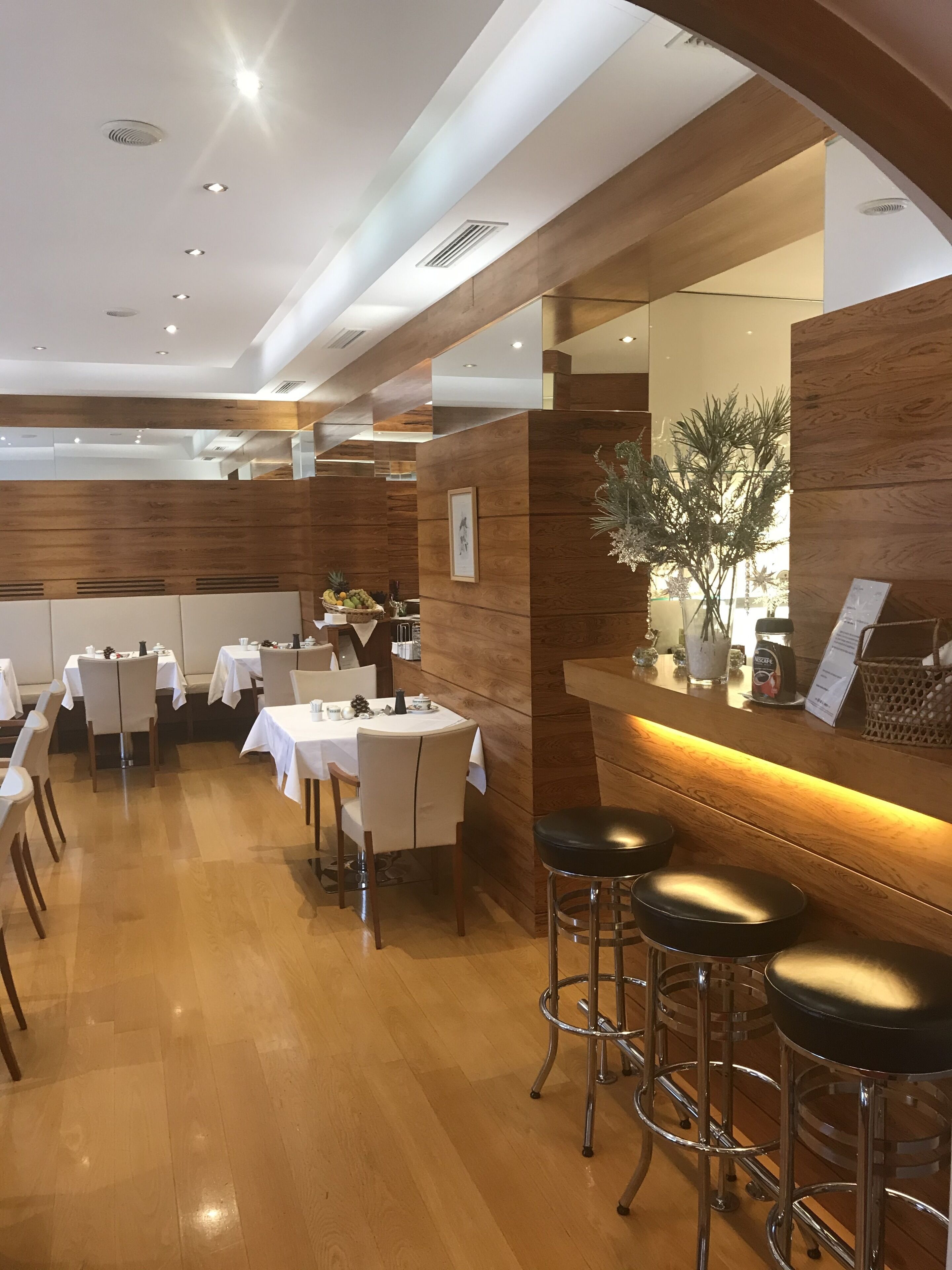 A restaurant with wooden paneling, white tables, and black bar stools.