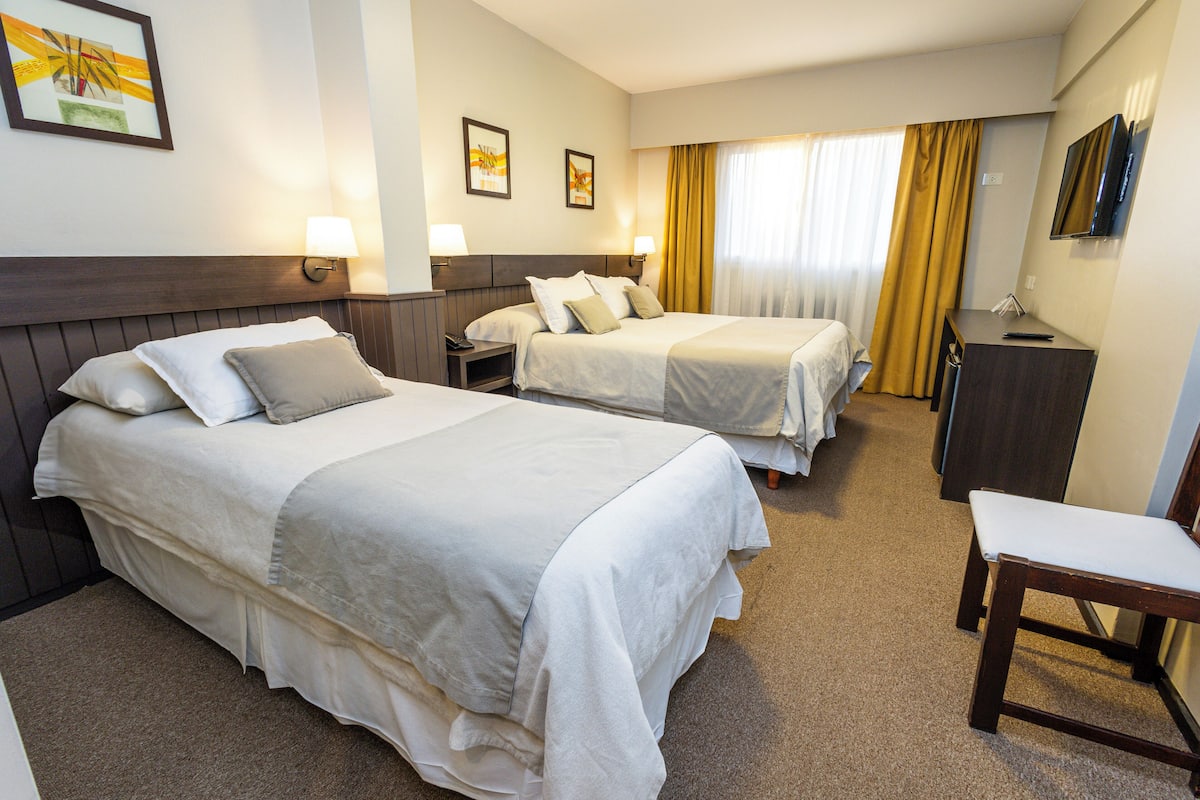 Une chambre d’hôtel avec deux lits, un bureau, une chaise et un téléviseur fixé au mur.