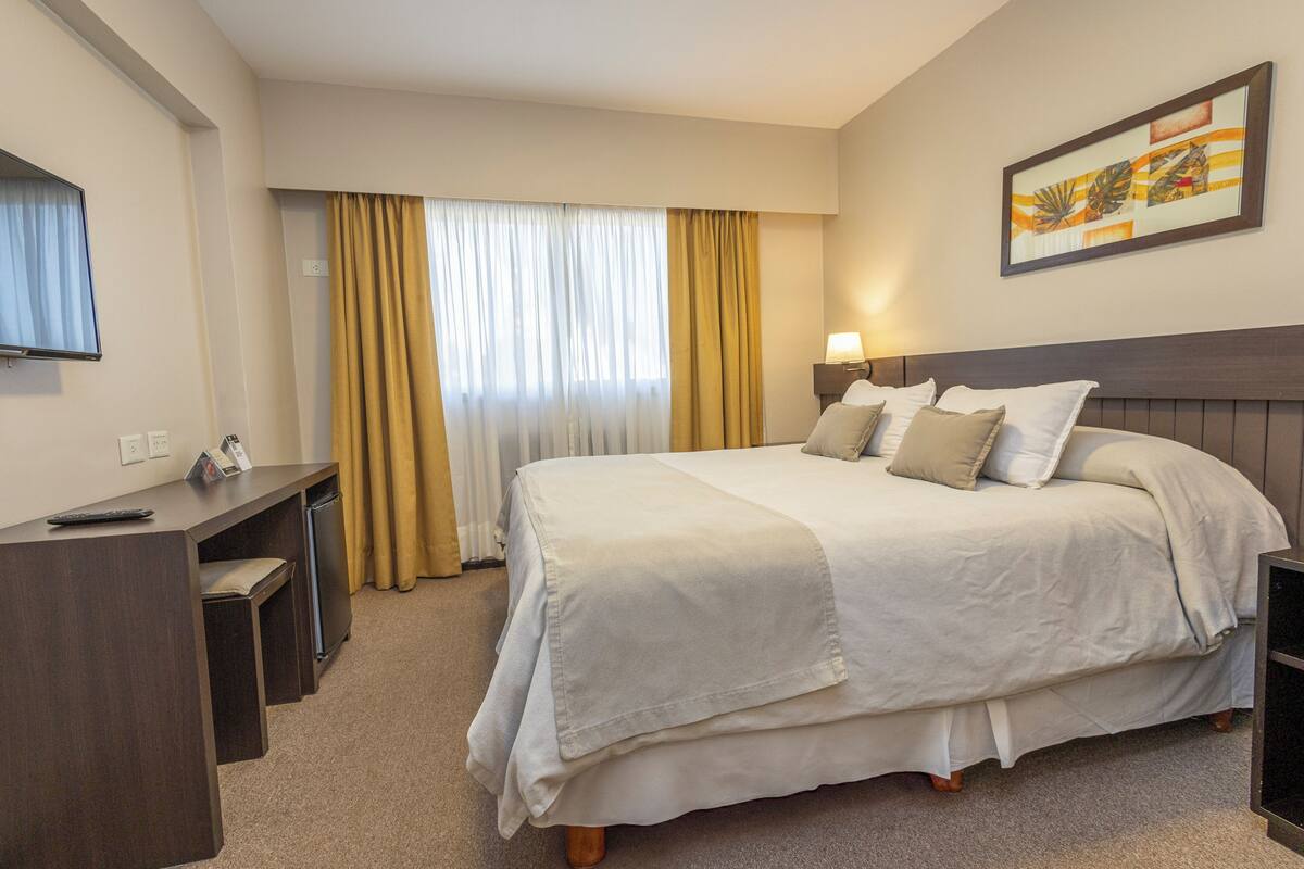 Une chambre d’hôtel avec un lit, un bureau, une télévision et un tableau au mur.