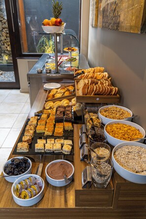 A buffet with various food items including pastries, fruits, and cereals.