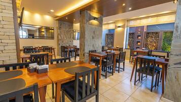 A restaurant with wooden tables and chairs, stone walls, and a large mirror.