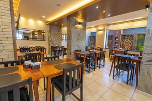 A restaurant with wooden tables and chairs, stone walls, and a large mirror.