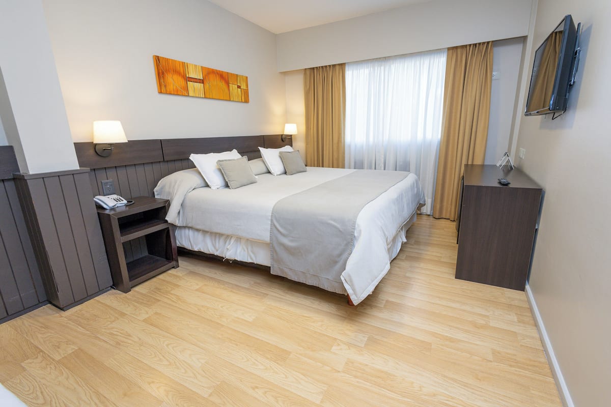 Une chambre d’hôtel avec un grand lit, des tables de chevet, un bureau, une télévision et un tableau au mur.