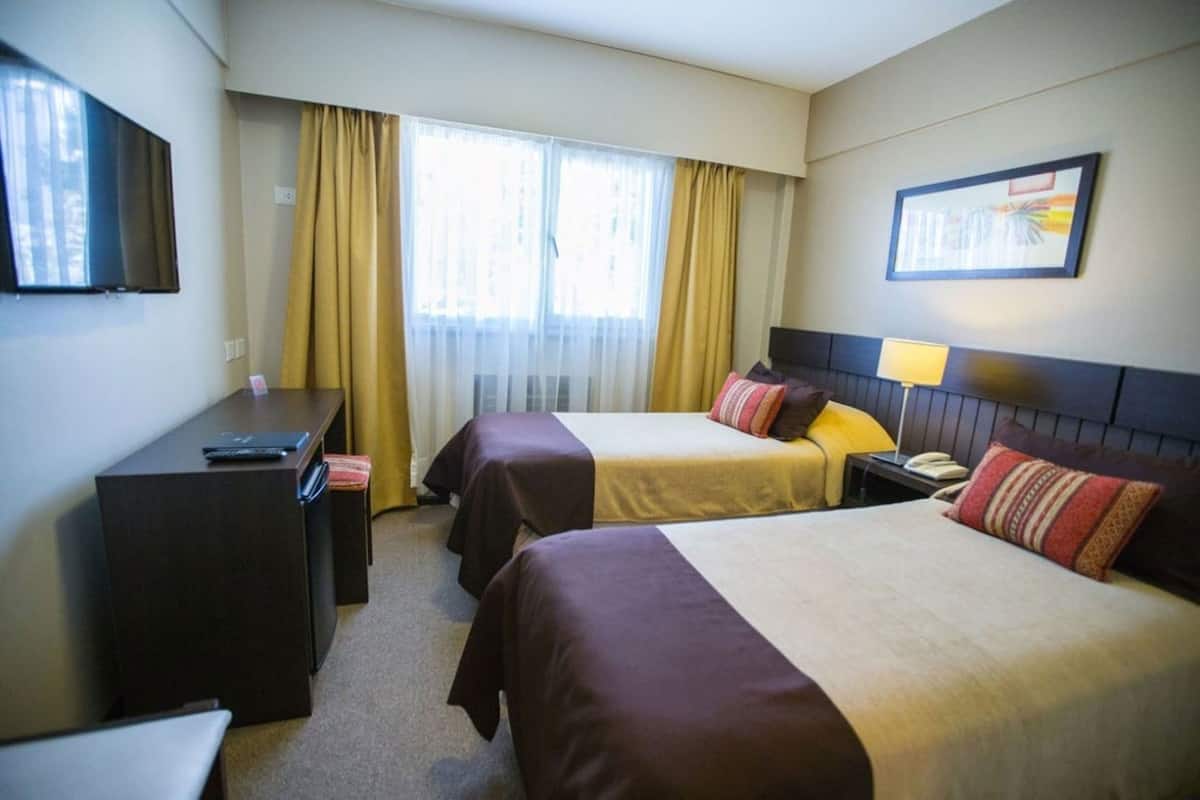 Une chambre d’hôtel avec deux lits, un bureau, une chaise, une télévision, un téléphone et une fenêtre avec des rideaux.