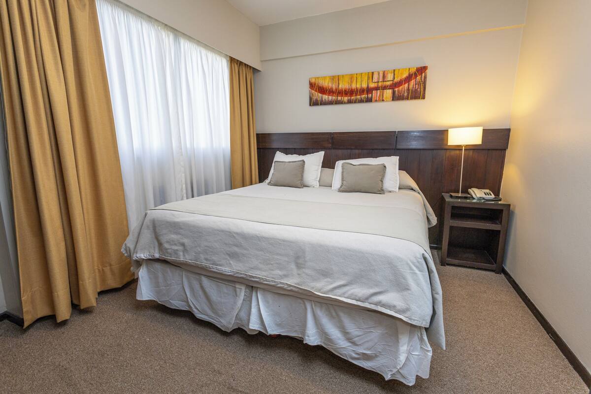 Une chambre d’hôtel avec un grand lit, une table de chevet avec une lampe et un tableau au mur.