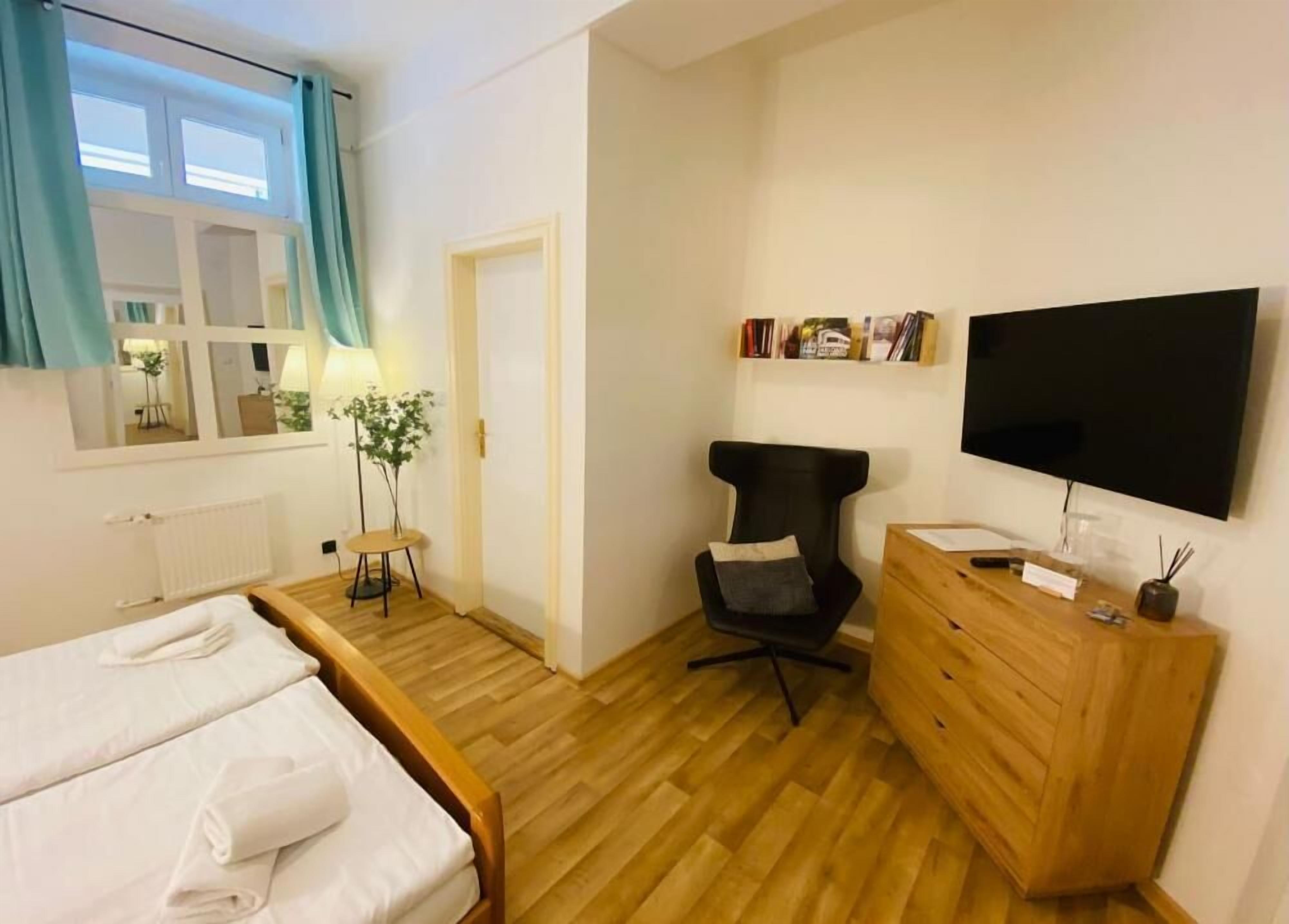 Et hotelværelse med en seng, et skrivebord, en stol, et fjernsyn og en trækommode.