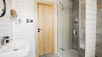 Un baño con puerta de madera, cabina de ducha de vidrio y lavamanos blanco.