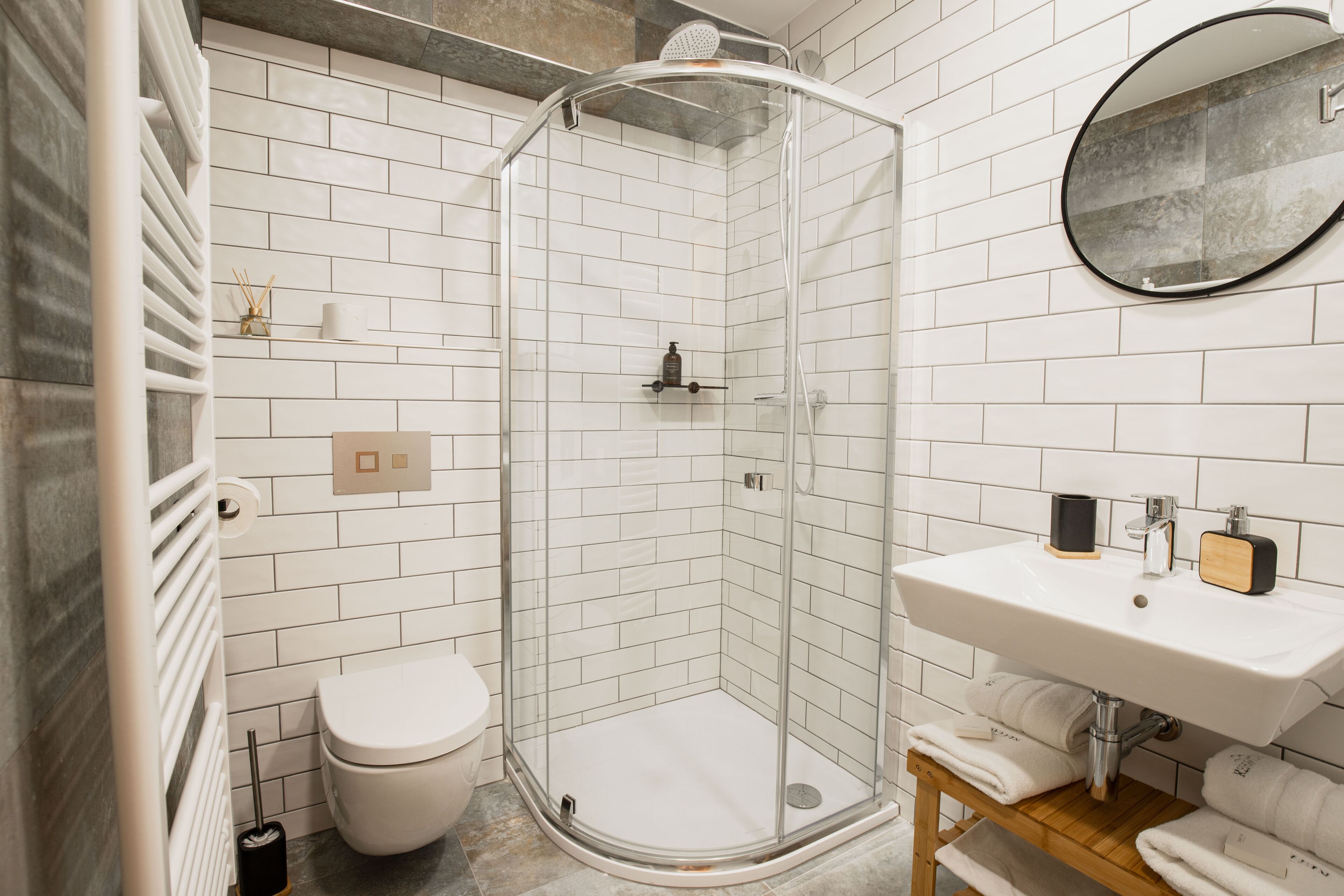 A modern bathroom with a glass-enclosed shower, white tiled walls, a white sink, and a wooden vanity.