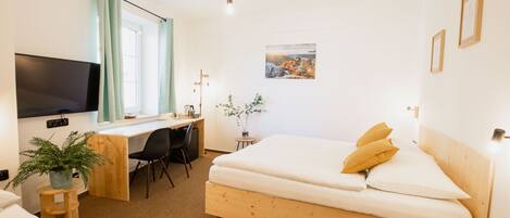A hotel room with a wooden bed, a desk with a chair, a television, and a window with curtains.