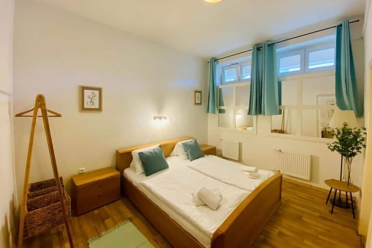 A bedroom with a wooden bed, a bedside table, a nightstand, a hanging chair, and a window with curtains.