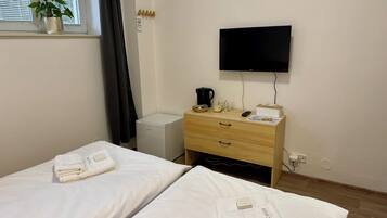 A hotel room with two beds, a TV, a small refrigerator, a wooden dresser, and a window with a plant.