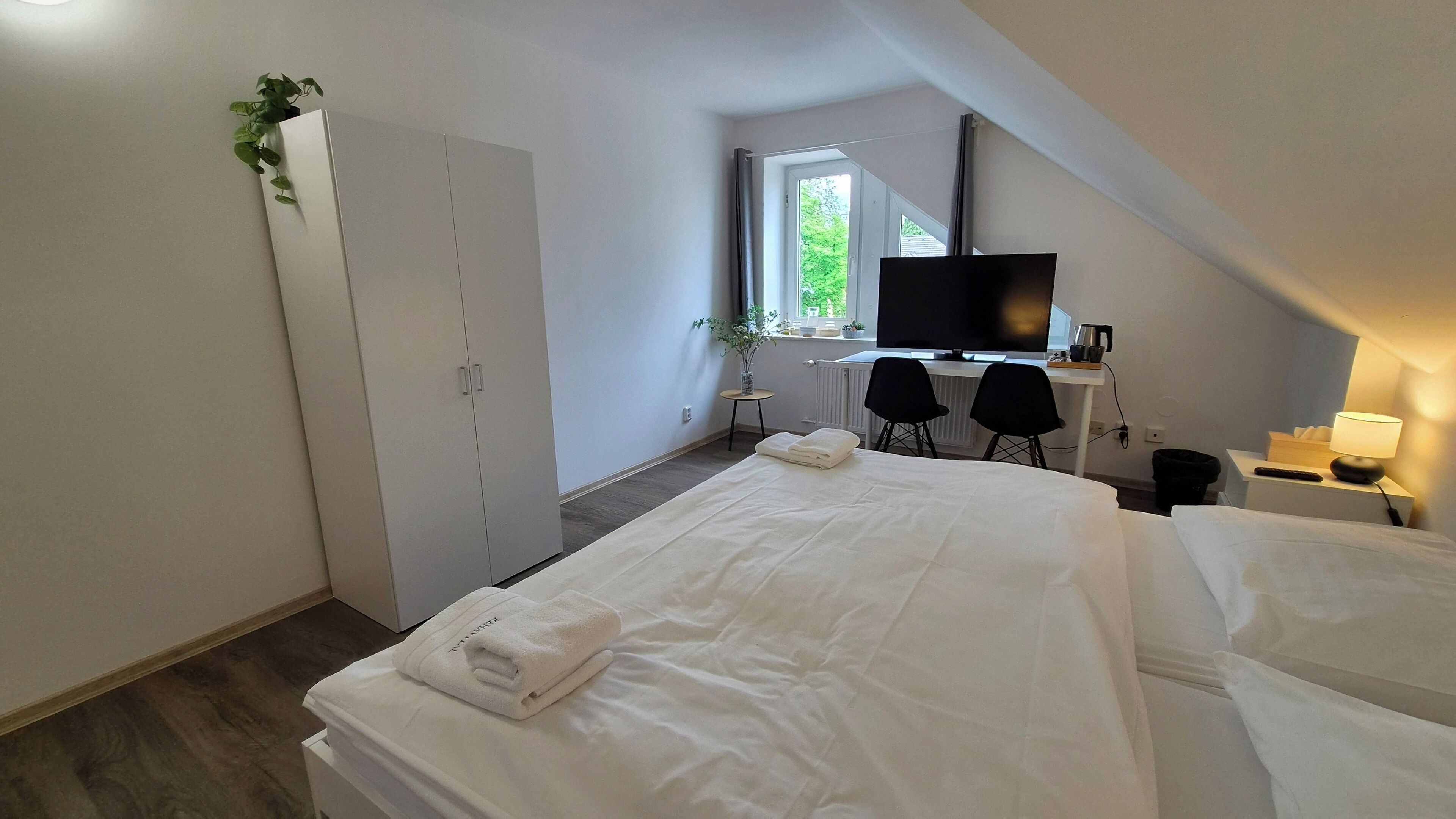 Una habitación de hotel con una cama, un escritorio con computadora, un televisor y una ventana.