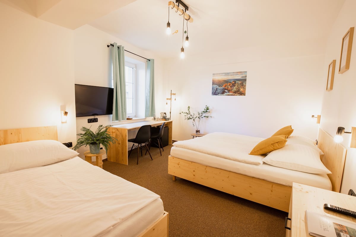 A hotel room with two beds, a desk with a chair, a TV, and a window with curtains.