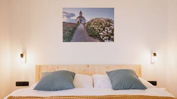 A bedroom with a wooden headboard, two pillows, a white bedspread, and a framed picture of a pathway leading to a building.
