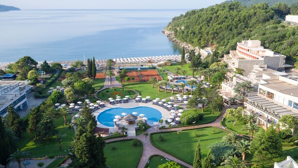 A resort with a central swimming pool, sun loungers, and a view of the sea.
