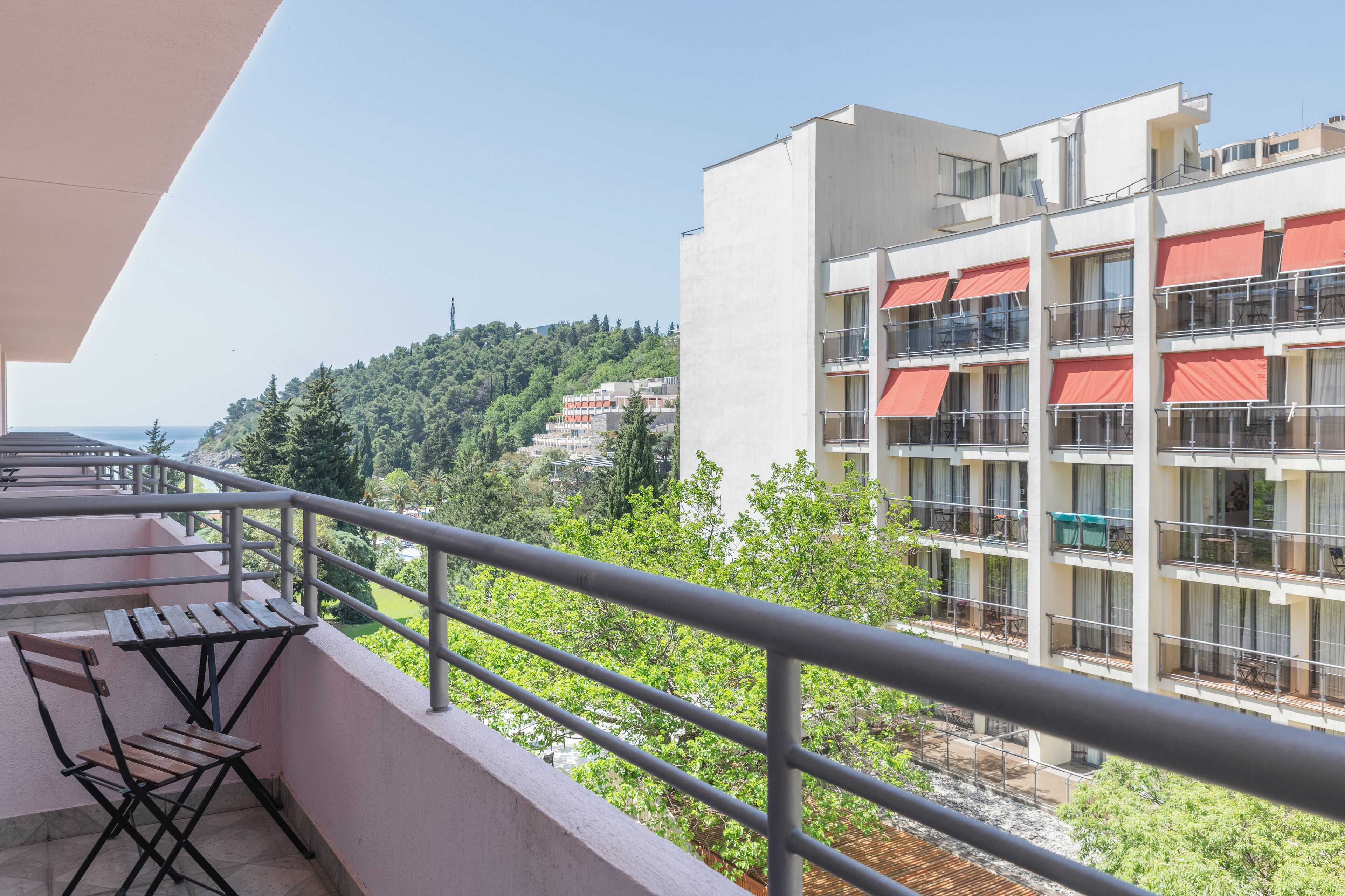 A balcony with a table and chairs, overlooking a building with multiple balconies and a view of a hillside.