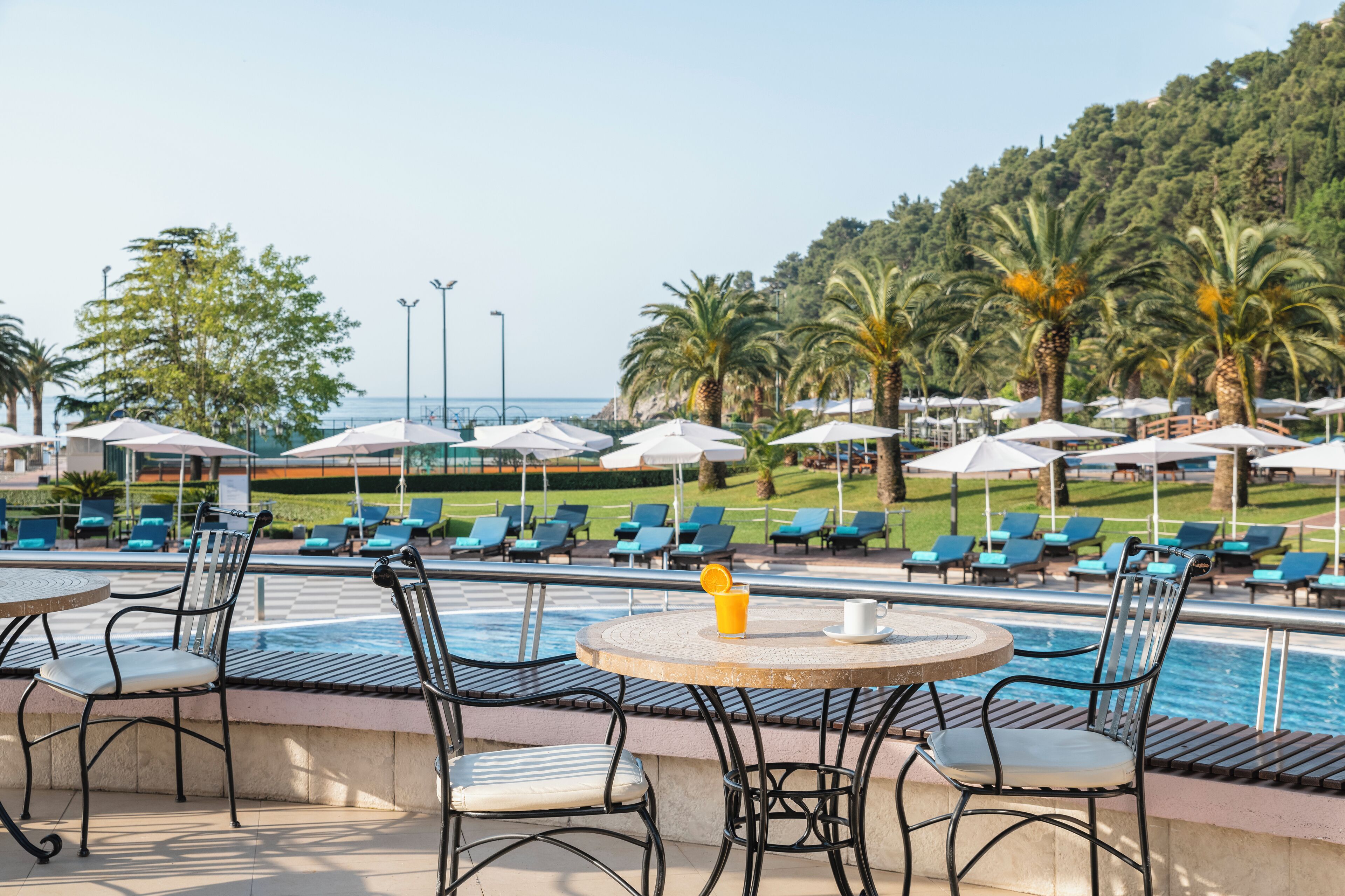 Zona junto a la piscina con sillas de descanso y sombrillas, una piscina y vistas al mar y al follaje.