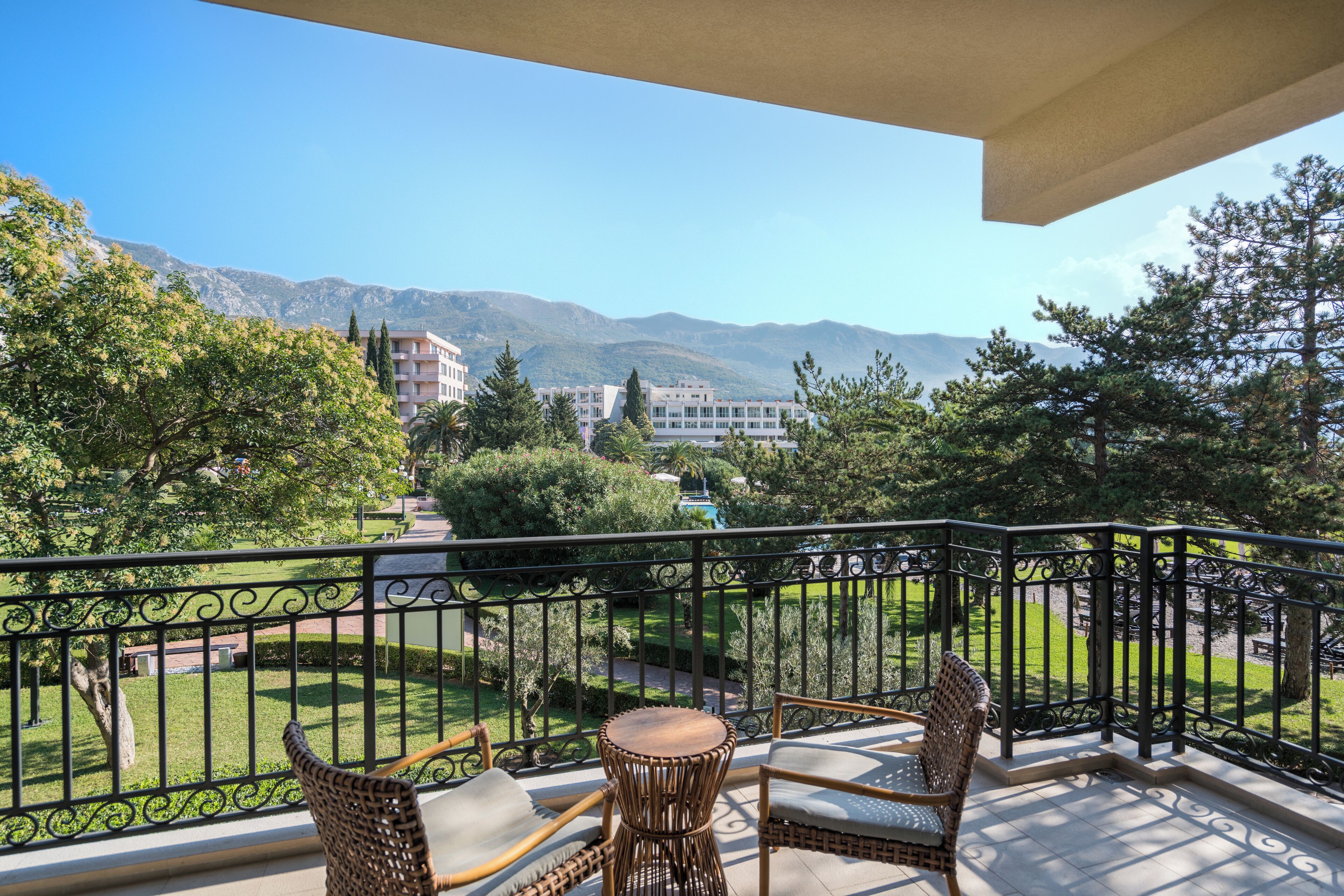 Un balcon agrémenté de meubles en osier, avec vue sur un jardin aménagé et des bâtiments en arrière-plan.