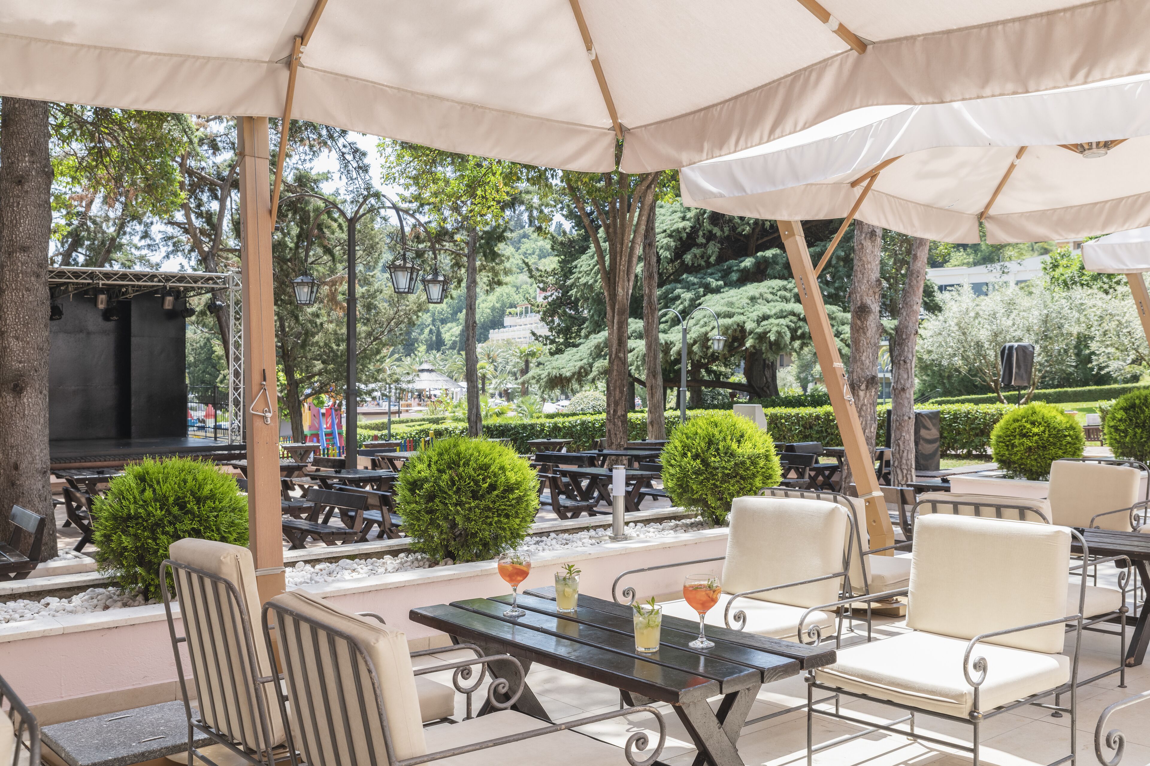 An outdoor patio with tables and chairs, surrounded by trees and a stage.