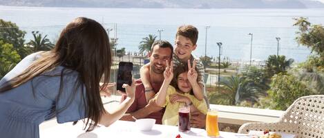 Eine Familie speist an einem Tisch mit Blick auf Meer und Berge.