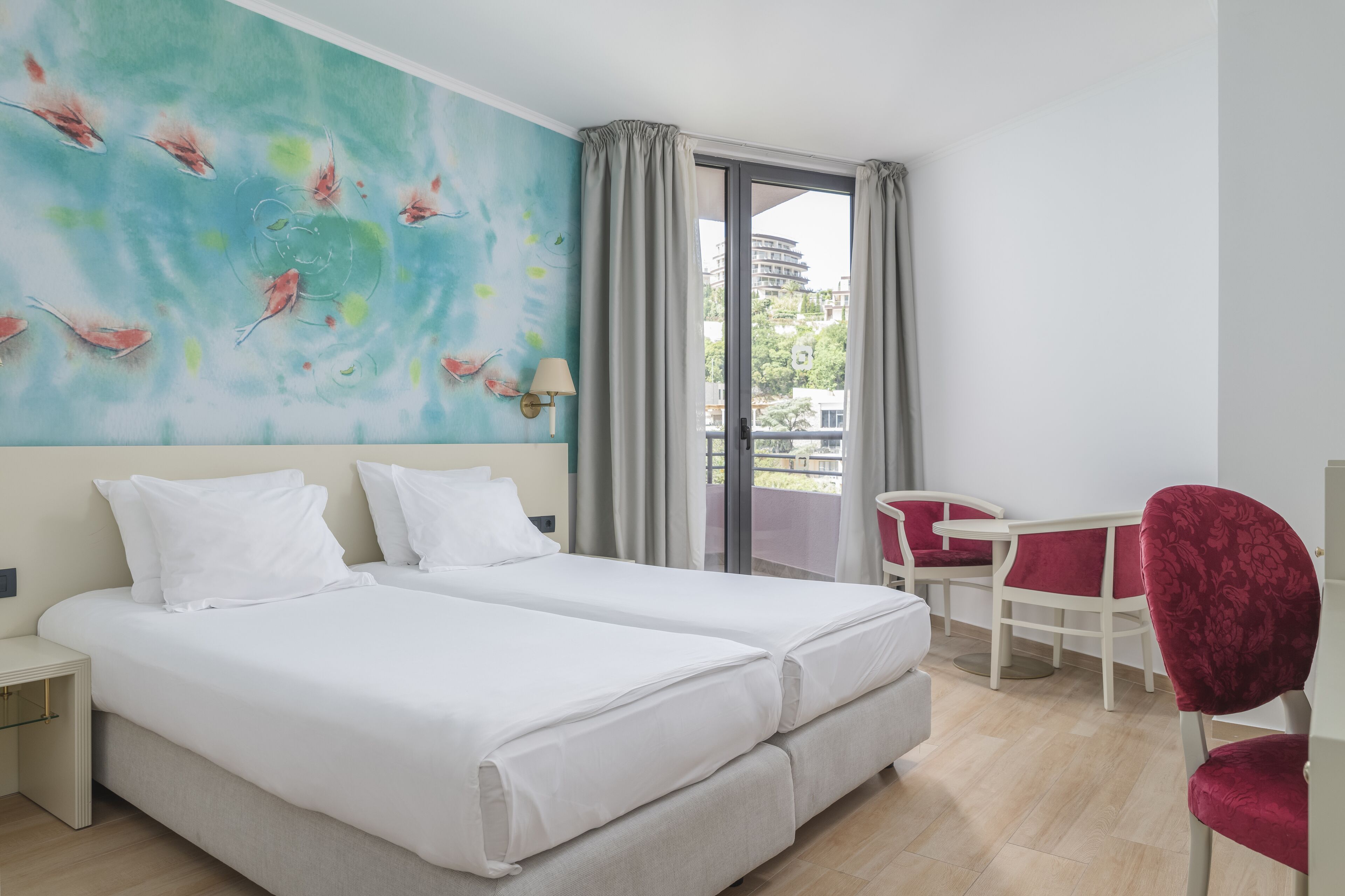 A hotel room with two beds, a dining area with a table and chairs, and a large window with curtains.
