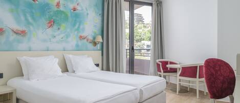 A hotel room with two beds, a dining area with a table and chairs, and a large window with curtains.