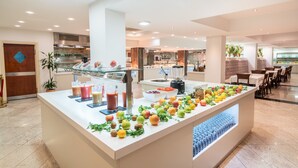 A modern hotel lobby with a central buffet area featuring a variety of fruits and beverages.