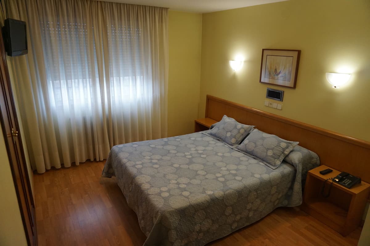 Habitación de hotel con cama, cabecera de madera, mesitas de noche, un control remoto y un aplique de pared.
