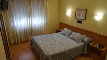 Habitación de hotel con cama, cabecera de madera, mesitas de noche, un control remoto y un aplique de pared.