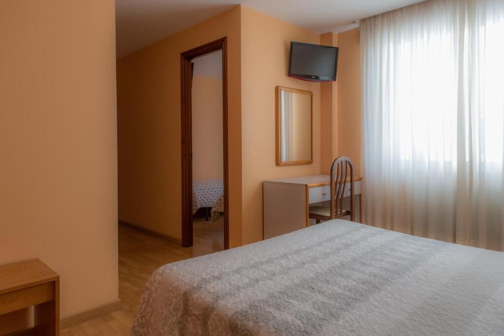 Habitación de hotel con cama, escritorio, silla, televisor y puerta que da a otra habitación.