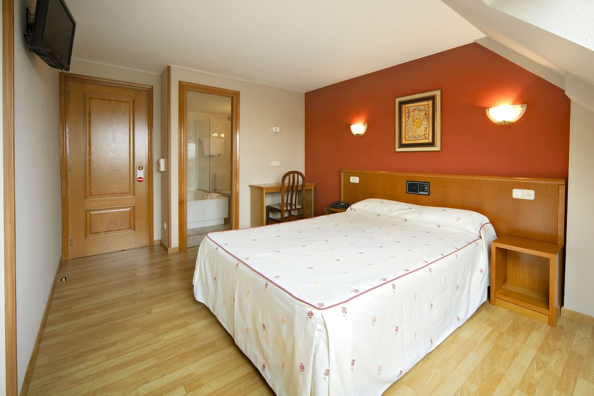 Un dormitorio con cama, escritorio, silla, ducha y televisión.