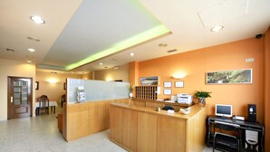 A reception area with a wooden reception desk, a computer, a printer, and a small plant. - Europa (Arteixo)