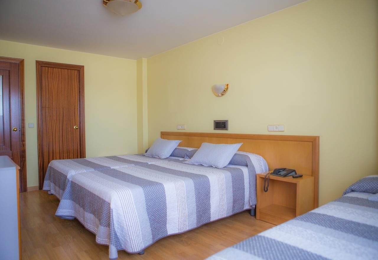 A hotel room with two beds, wooden headboards, a bedside telephone, and a wall clock.