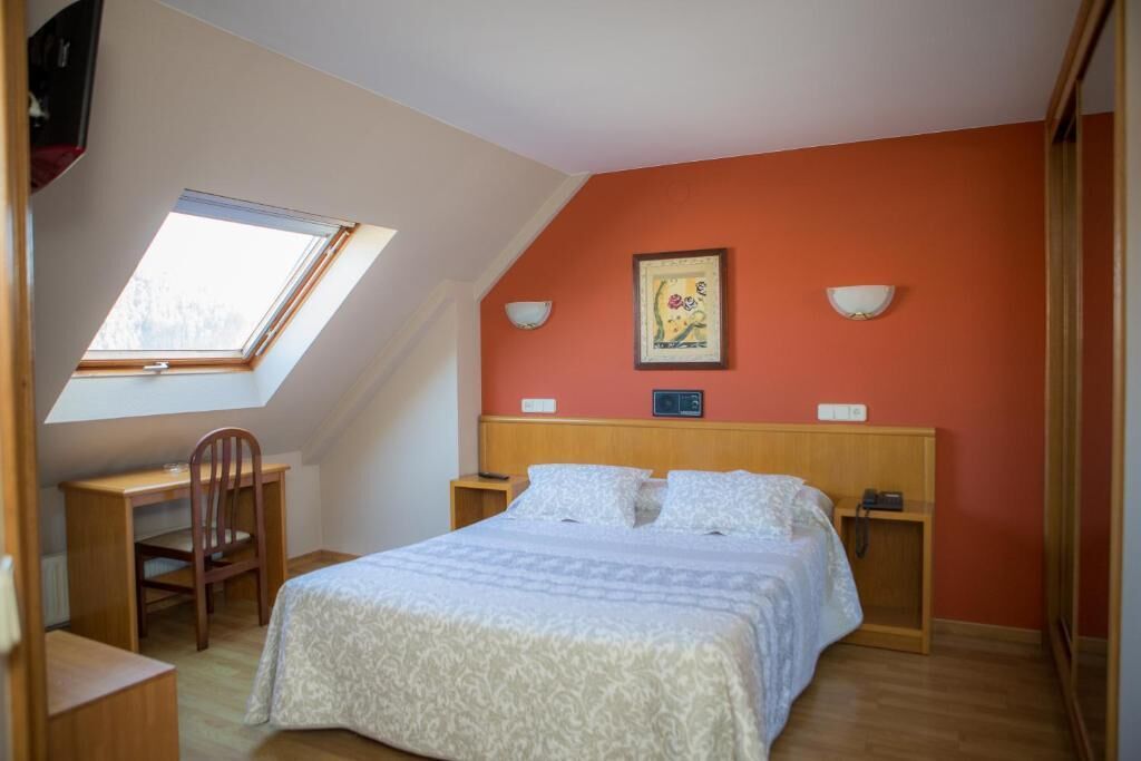 A bedroom with a sloped ceiling, a bed, a desk, and a chair.