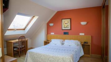 A bedroom with a sloped ceiling, a bed, a desk, and a chair.