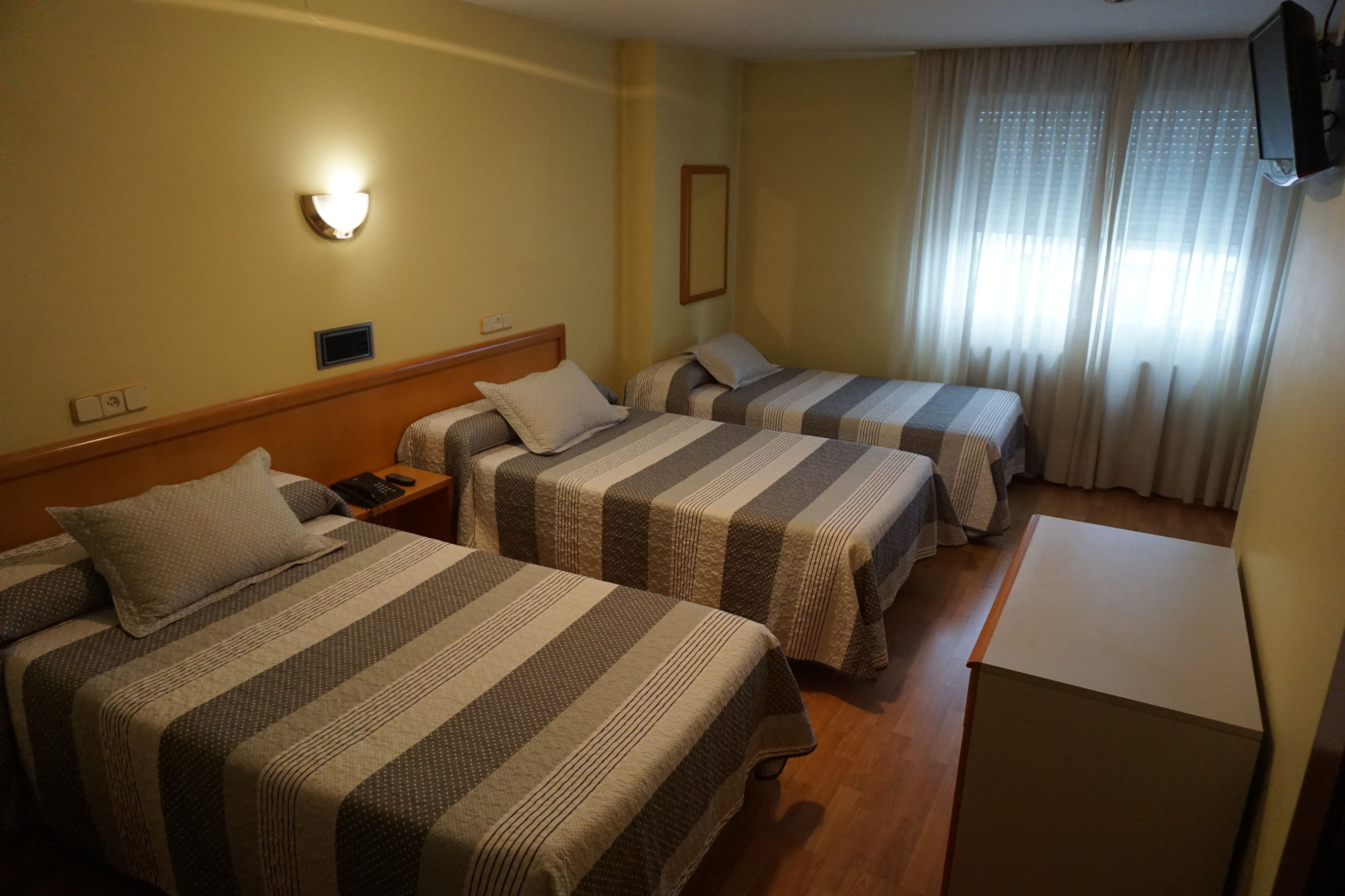 A hotel room with two beds, a nightstand, a TV, and a window with curtains.