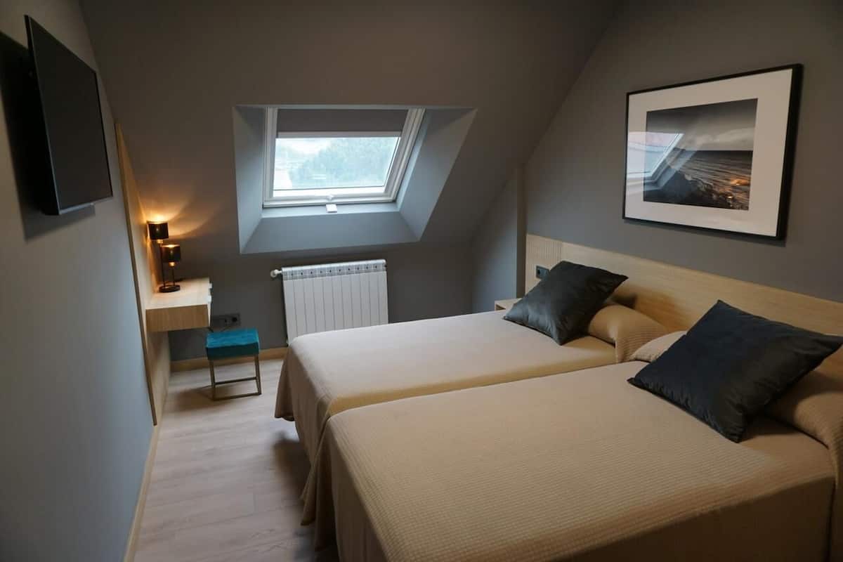 Un dormitorio con dos camas, un tragaluz, un escritorio y un cuadro en la pared.