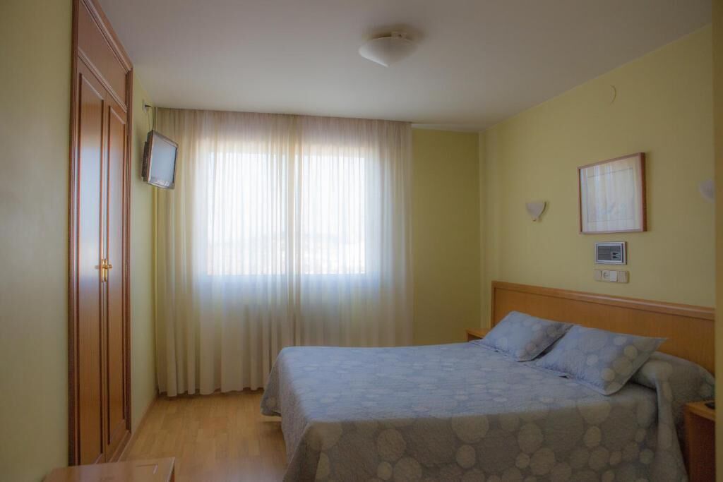 Ein Zimmer mit zwei Betten, einem Fernseher und einem Fenster mit Vorhängen.