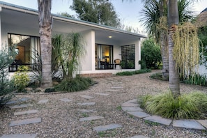A modern house with a covered porch, a gravel pathway, and various plants. - De Old Drift Guest Farm (Addo)