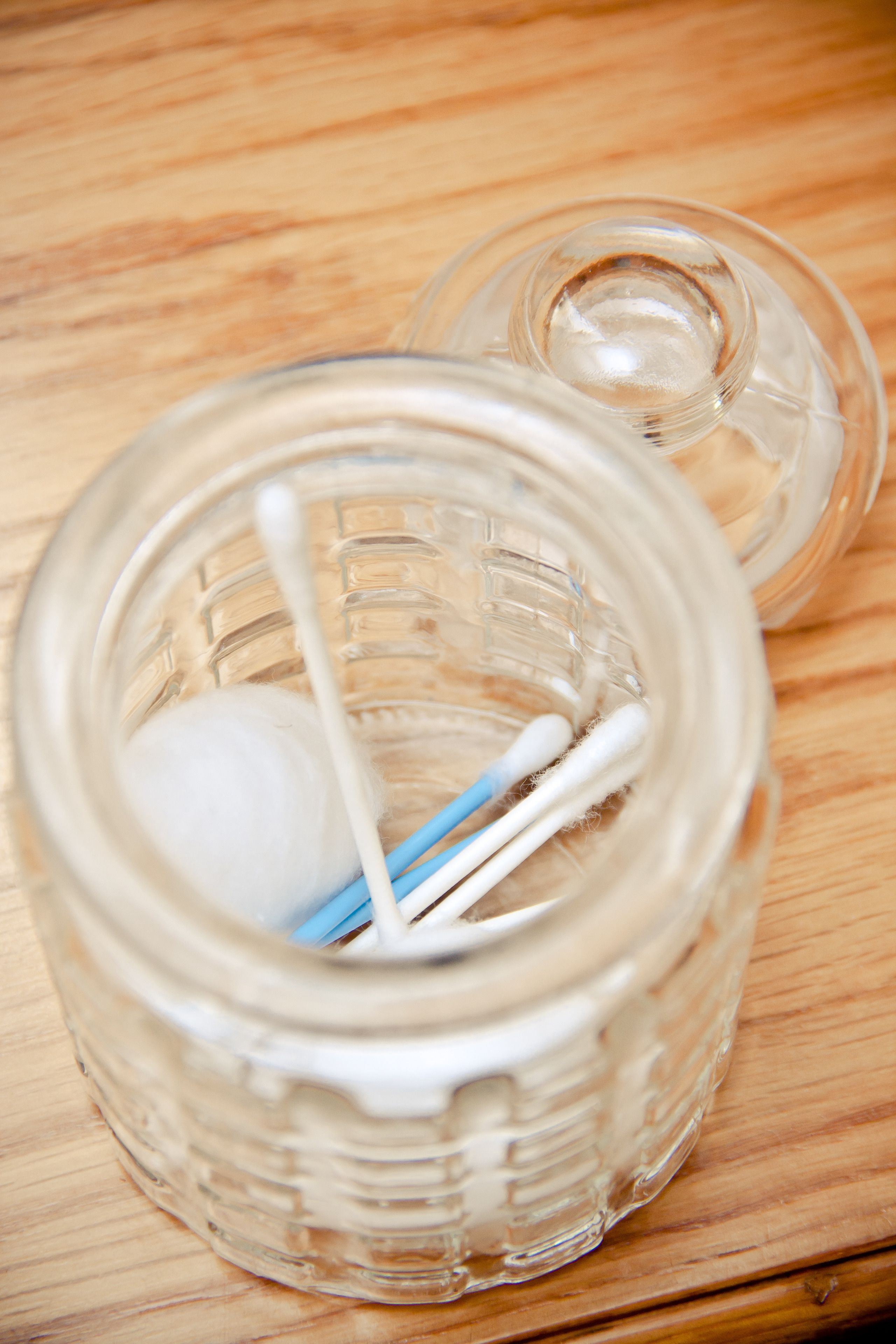A clear glass jar with cotton swabs and a cotton ball on a wooden surface.